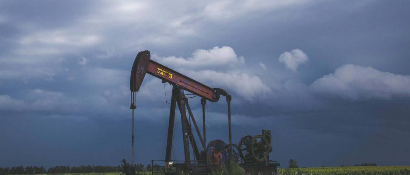 A red oil pump in a grass field with grey, cloudy overcast above