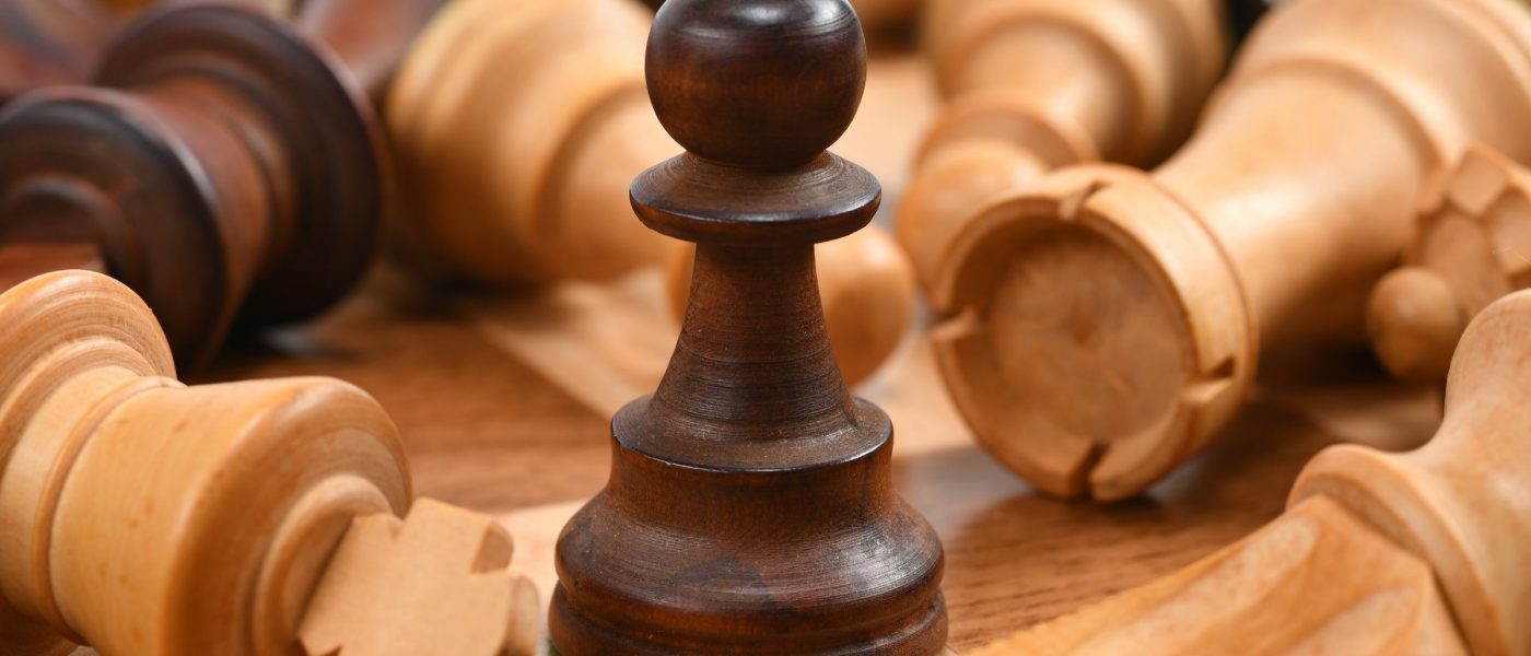 Pawn chess piece standing among fallen chess pieces
