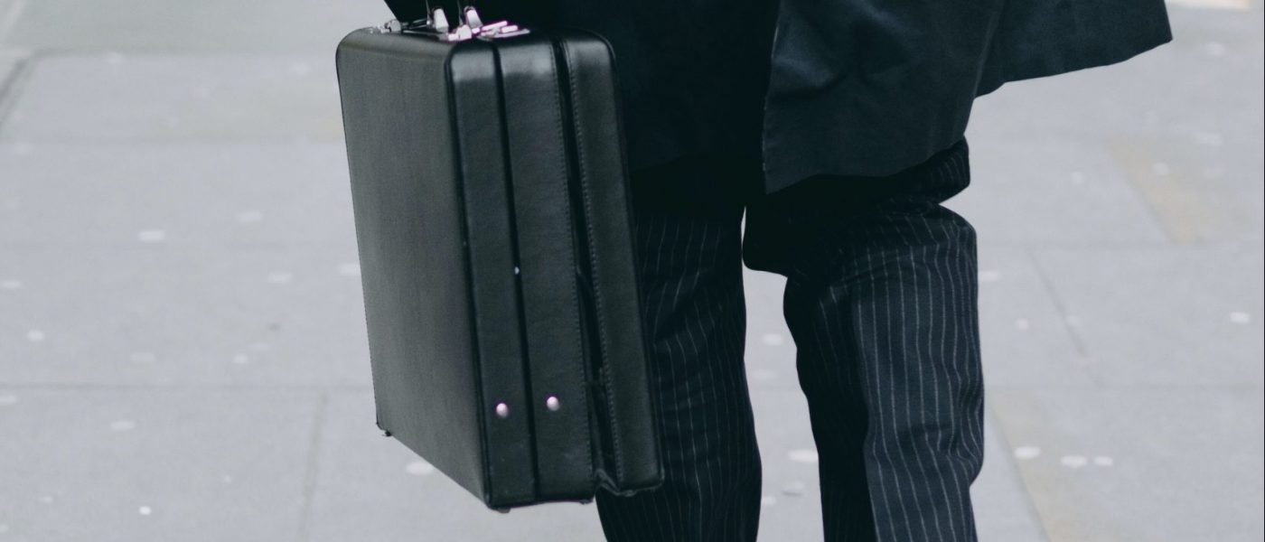 Business man in pin stripe suit carrying a black briefcase walking down a sidewalk