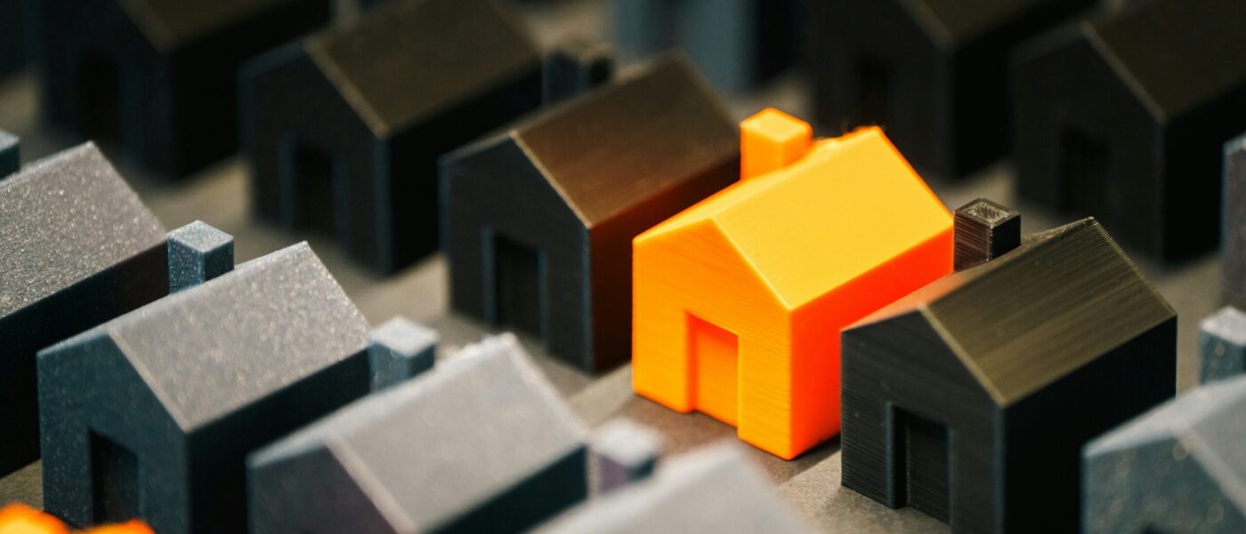 A miniature 3D printed orange house in a row of black miniature 3D printed house A miniature 3D printed orange house in a row of black miniature 3D printed house