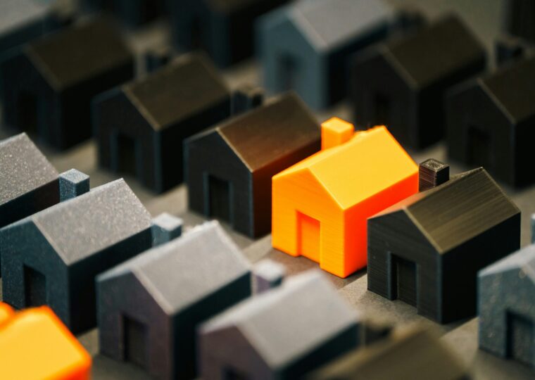 A miniature 3D printed orange house in a row of black miniature 3D printed house