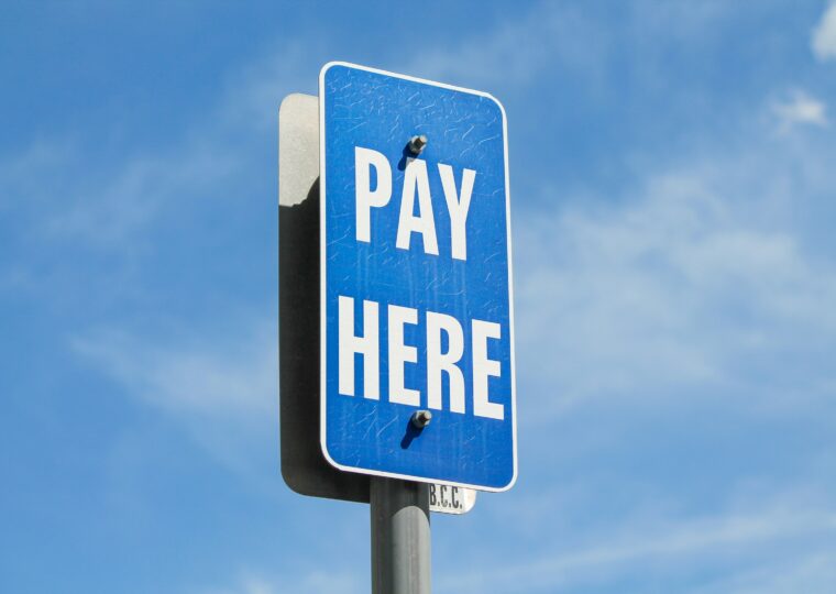 A blue street sign that says 'pay here' on a sunny day