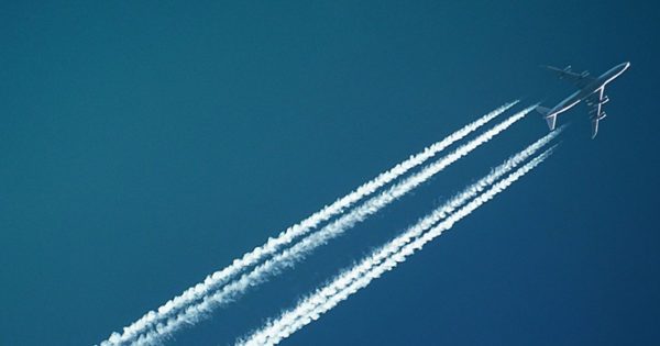 A plane cuts diagonally across a deep blue sky, leaving contrails behind it