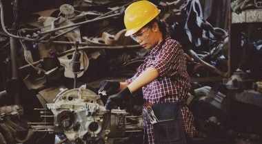 woman engineer working on engine in factory wearing a heard helmet