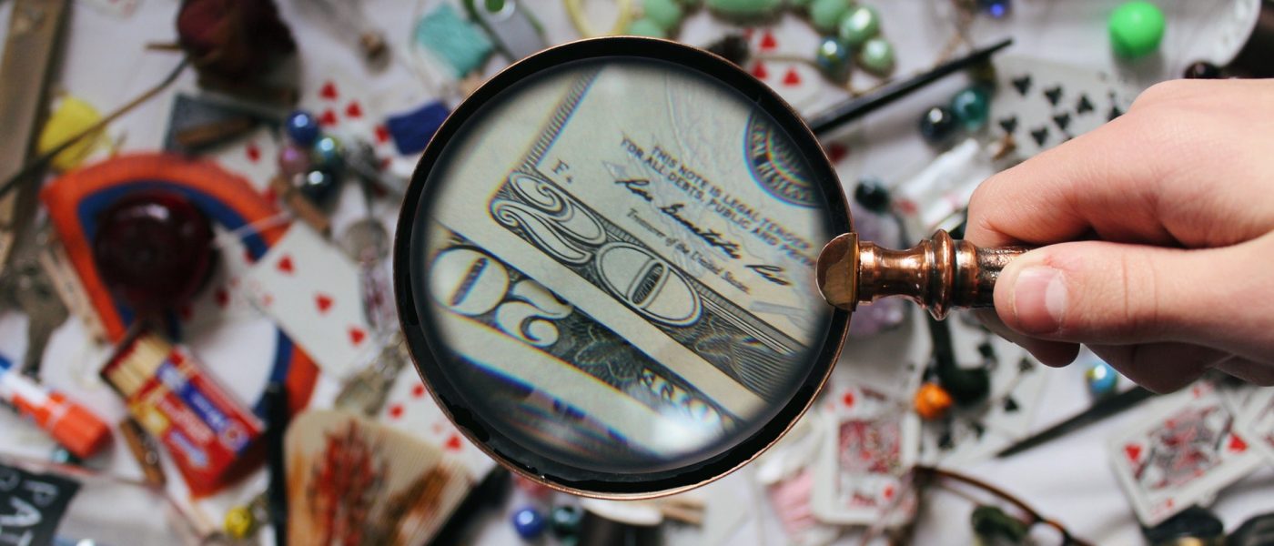 Magnifying glass spotting dollar bills amid a mess of objects