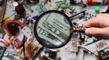 Magnifying glass spotting dollar bills amid a mess of objects