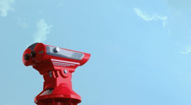 A red coin operated binocular against a bright blue sky