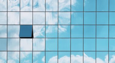 A single open window in a grid of closed glass windows mirroring the sky