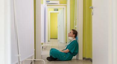 A tired nurse sits on the floor of a hallway